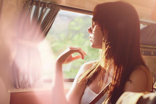 A carefree young woman in her camper van enjoying the warmth of the sun. Young woman on a road trip sitting in her van enjoying the sun. Content young woman sitting in her camper van on a road trip