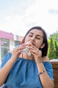 Stylish millennial woman eating burger at street cafe in summer