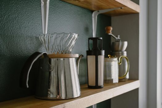 Set of coffee preparation with pour over brewer, manual coffee grinder and kettle on wooden shelf.