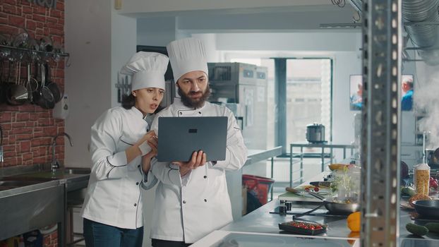 Team of cooks working on professional cusine meal with laptop