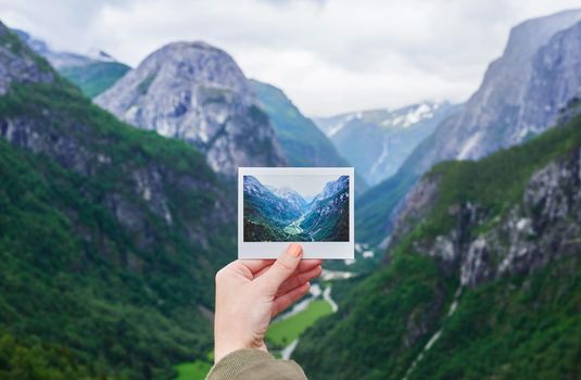 Hand holding up polaroid instant photo of travel destination glacial valley wanderlust inpiration concept