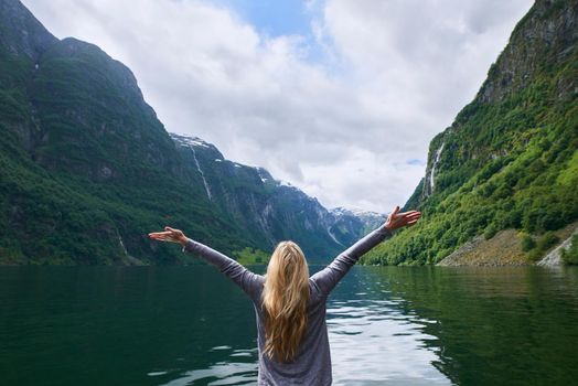 Travel adventure woman celebrates arms raised at view of majestic glacial valley fjord lake on exploration discover beautiful earth