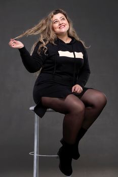 A beautiful fat woman with long curly hair sits on a chair.