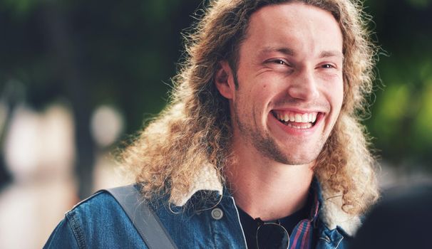 A cheerful handsome man with curly hair in the park. A happy young man laughing relaxing outside in the park. A young handsome man with blonde curly hair spending time in the garden