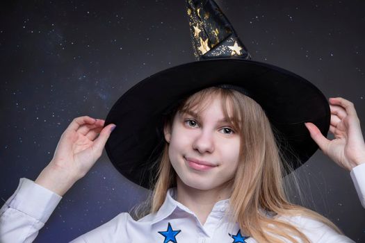 A funny teenage girl wearing a Hallow hat is shot against a starry background looking at the camera and smiling.