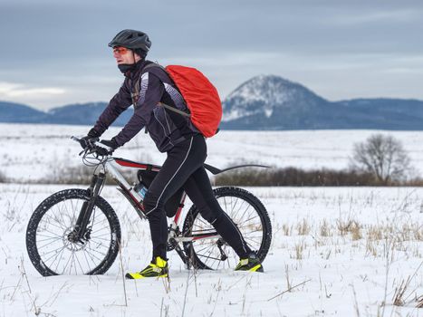 Adult athlete pushes MTB through the snow across a frozen meadow.