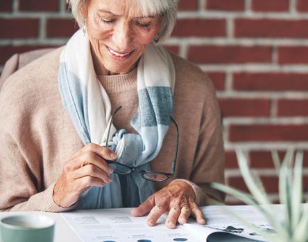Senior woman reading retirement contracts. Mature woman sitting down reading financial paperwork. A happy mature woman holding her glasses reading over legal documents