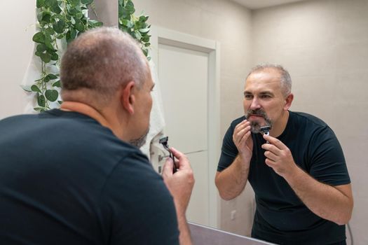 Middle-aged handsome man using razor in bathroom