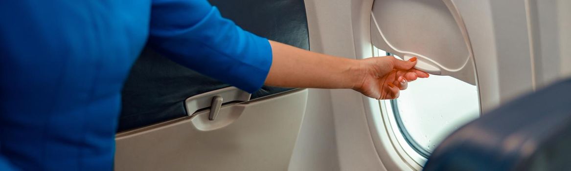 Woman flight attendant closing window in airplane