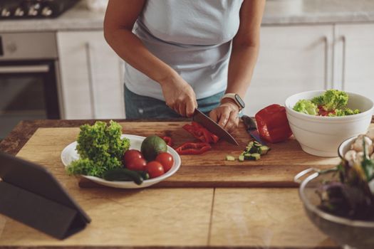 A woman cuts vegetables for a salad on a wooden kitchen board