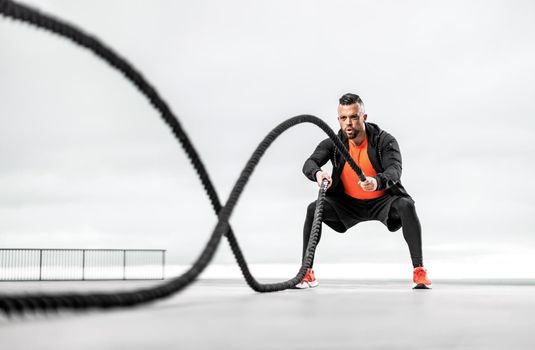 Athletic man with a battle rope doing sports exercises on the ocean