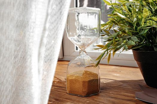 Hourglass with golden sand pouring inside on wooden background