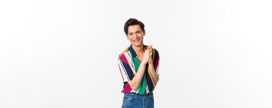 Attractive young slim man relish something good, rubbing hands and smiling satisfied, standing over white background