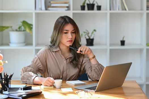 Concentrated attractive businesswoman working with laptop at modern office.