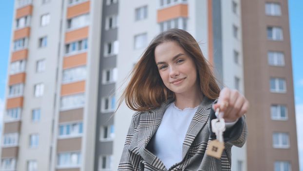 The girl shows the keys to the apartment against the backdrop of an apartment building.