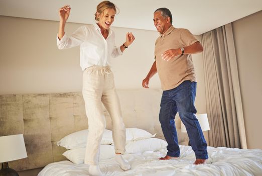 Senior interracial couple jumping on a hotel bed and having fun together. Senior man and woman full of energy and life. They are celebrating and enjoying their honeymoon