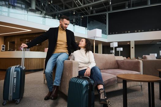Charming heterosexual married couple, business partners, passengers with suitcases relaxing in the VIP lounge, waiting for flight check-in at international airport