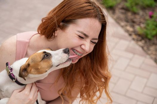 Dog jack russell terrier licks the owner in the face outdoors.