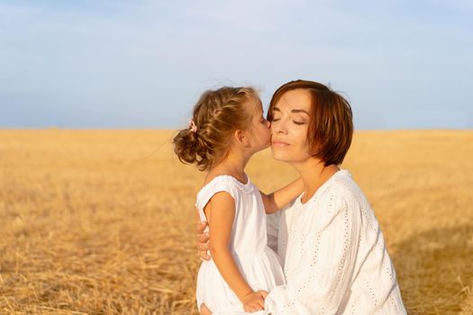 Daughter kisses her mom cheek standing wheat field