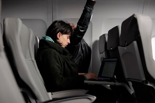 Young adult working on laptop during airplane flight abroad