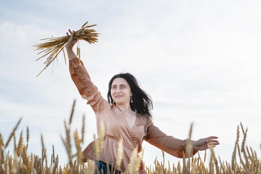 Mid adult woman in beige shirt standing on a wheat field with sunrise on the background, back view