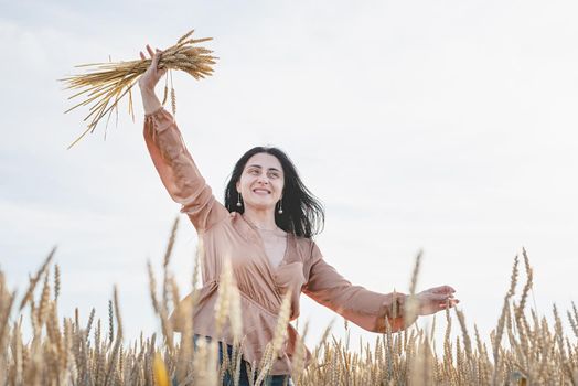 Mid adult woman in beige shirt standing on a wheat field with sunrise on the background, back view