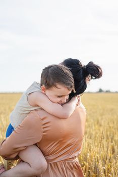 Happy family of mother and infant child walking on wheat field, hugging and kissing