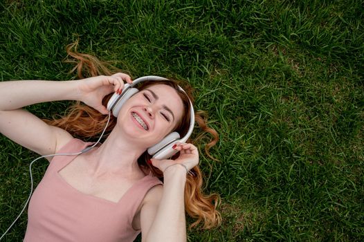 A young red-haired woman lies on the grass and listens to music.