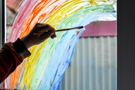 hand painting rainbow on a window, stay home during quarantine