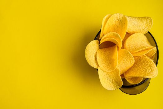 Delicious Crispy potato chips in bowl on yellow background