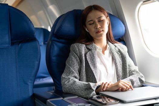 Tired business asian lady napping on seat while traveling by airplane. Commercial transportation by planes