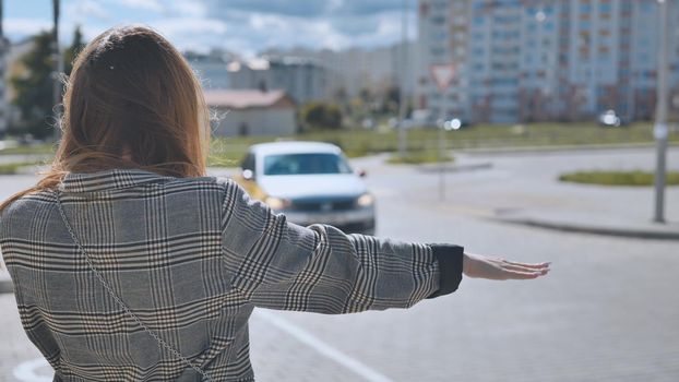 A girl is waving to a cab in the city.