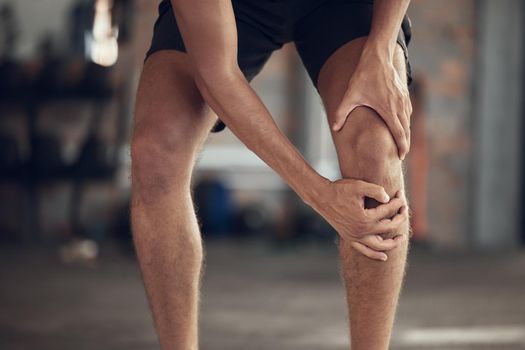 Closeup of athlete knee joint pain. Hands of fit man touching his knee in pain. Strong man with a sore knee in the gym. Bodybuilder with a hurt knee injury. Active man with a knee sprain