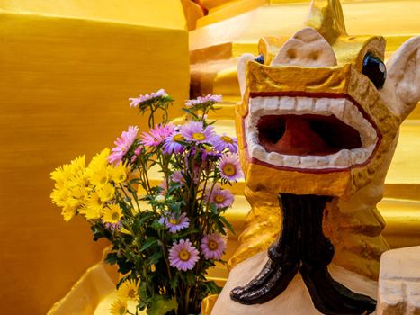 A bouquet of flowers for worship and a Burmese art lion statue at the base of the pagoda