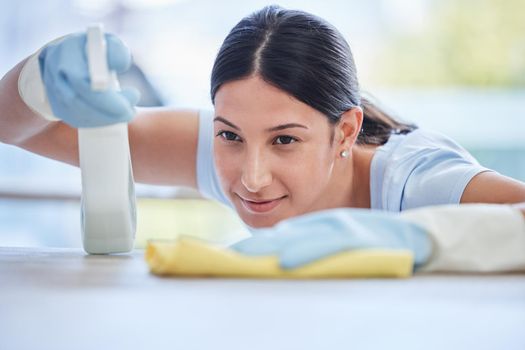 One beautiful smiling young mixed race woman cleaning the surfaces of her home. Happy Hispanic domestic worker wiping a table