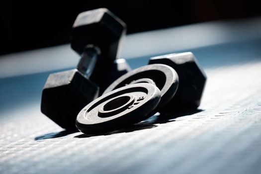Closeup of a group of gym weights on the floor in an empty health and sports club. Macro view of dumbbells barbell weights in a dark exercise room. Lift weight for body strength, muscles and fitness