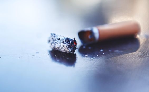 Closeup of dying cigarette butt lying on the floor. Smoking is addictive, unhealthy and may cause cancer. Stop smoking and quit bad habits.Tobacco smoke contains harmful chemicals as nicotine and tar
