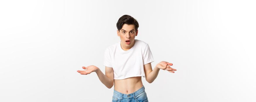 Lgbtq community. Confused gay man in crop top shrugging and staring at camera, cant understand, standing over white background
