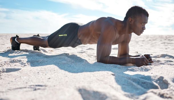 Fit young black man doing plank hold exercises on sand at the beach in the morning. One muscular male bodybuilder athlete with six pack abs doing bodyweight workout to build strong core and endurance