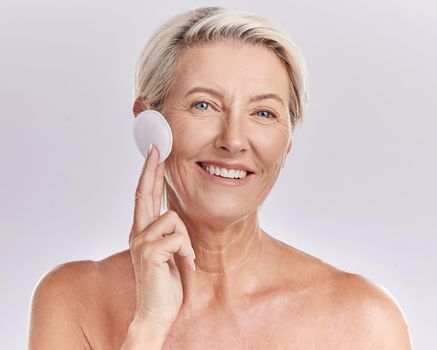 Portrait of a mature caucasian woman using a cotton pad to remove makeup during a selfcare grooming routine. Older model applying cleanser to her face against pink copyspace background