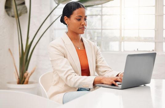 Young mixed race businesswoman working on a laptop at a table in an office at work. Serious hispanic businessperson typing on a laptop while working in corporate