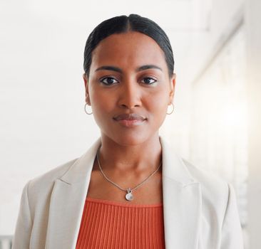 Young mixed race businesswoman standing alone in an office at work. Face of one confident hispanic businessperson looking serious standing at work