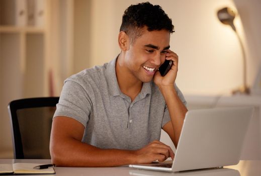 One young mixed race business man multitasking by talking on a cellphone and using a laptop to browse the internet. Happy, ambitious entrepreneur using technology to work on a startup in the evening