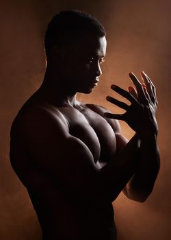 A handsome, muscular young african american man in studio against a dark background. A macho male athlete looking thoughtful isolated on black. Exercising body and mind. A question of mental health