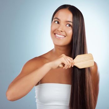 A beautiful young mixed race woman brushing her healthy strong hair and smiling against a grey studio background. Hispanic female grooming her hair