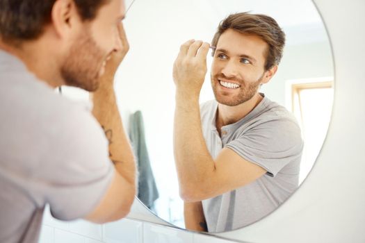 One handsome man tweezing his brow hair in a bathroom at home. Caucasian male using tweezer while looking in a mirror in his apartment