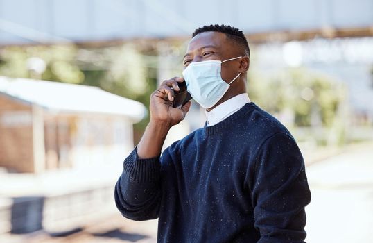 Black businessman wearing a face mask and talking on a cellphone outdoors. Making a call while commuting during the covid pandemic