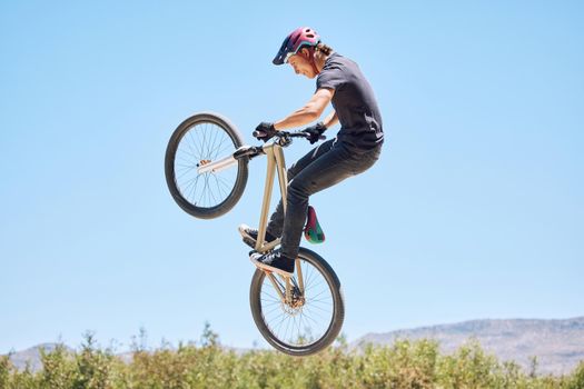 Young man showing his cycling skills while out cycling on a bicycle outside. Adrenaline junkie practicing a dirt jump outdoors. Male wearing a helmet doing tricks with a bike. Passionate and energetic