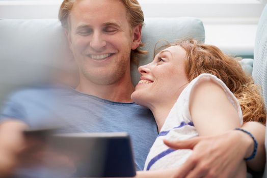 A smiling young couple resting on their couch while using a digital tablet. A smiling young couple resting on their couch while using a digital tablet.