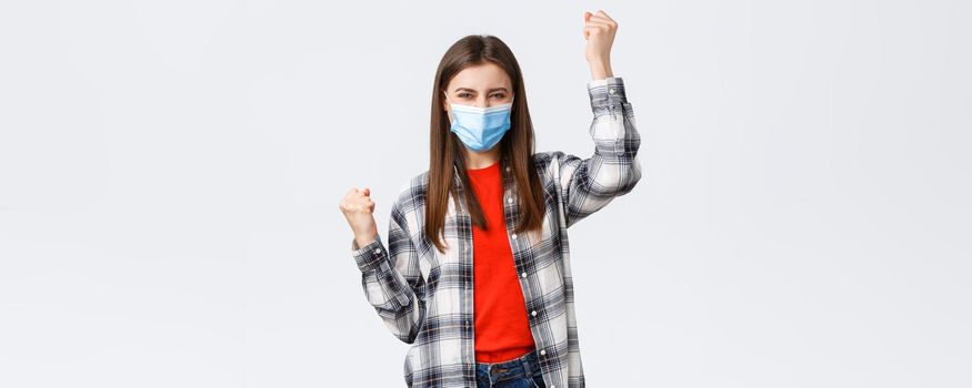 Different emotions, covid-19 pandemic, coronavirus self-quarantine and social distancing concept. Excited charismatic young woman in medical mask celebrate victory, dancing in rejoice, raise hands up